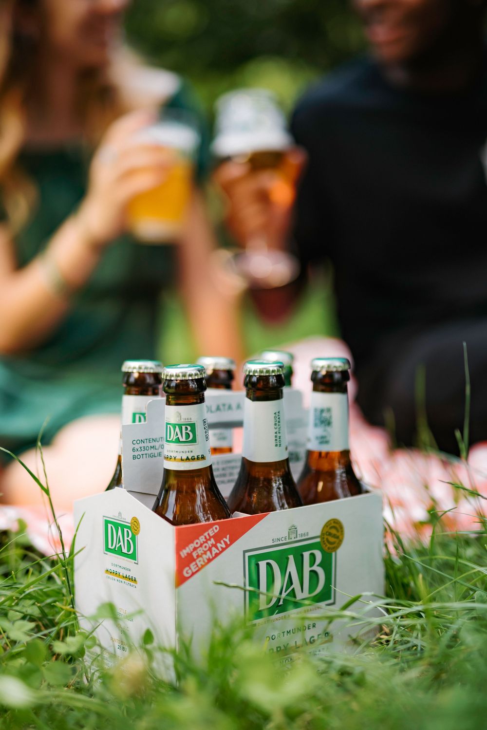 Beer bottles of DAB brand arranged in green grass on a sunny day, creating a refreshing outdoor scene.