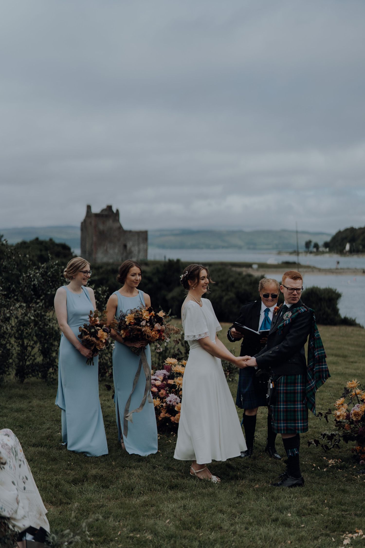 Wedding ceremony on Scottish coast with castle and water views in background.