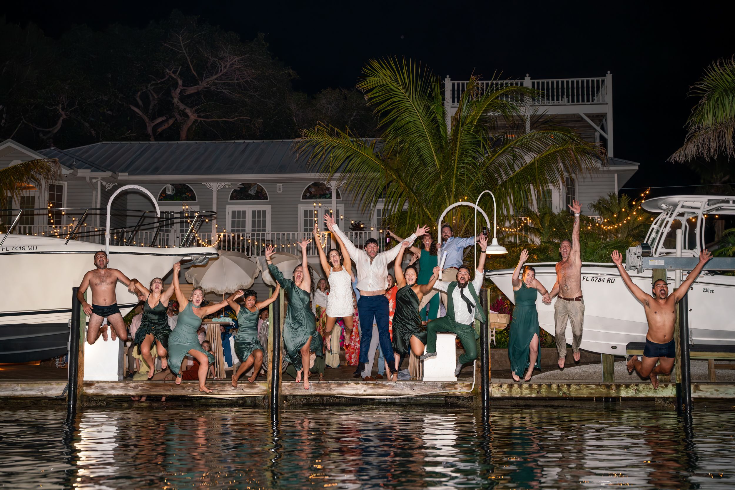 Group of wedding guests jump into a pool at night during celebration.