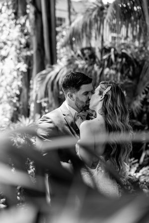 A romantic couple shares an intimate kiss in a lush tropical garden setting.