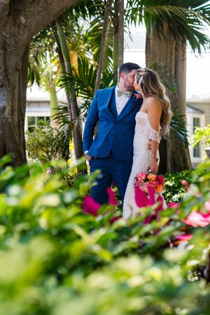 A couple shares a romantic moment in a lush tropical garden with palm trees and colorful flowers.