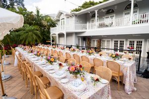 Elegant outdoor wedding reception setup with wooden tables and chairs on a white veranda.