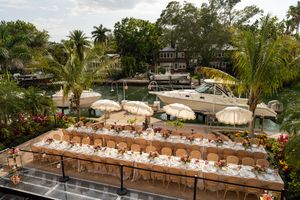 Long rustic wooden tables set for outdoor wedding reception under palm trees.