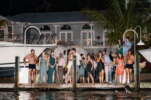 Wedding party poses on wooden dock by waterfront at sunset.