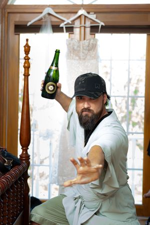 A bottle of champagne and a wedding dress hanging in a window with a decorative wooden post in the foreground.