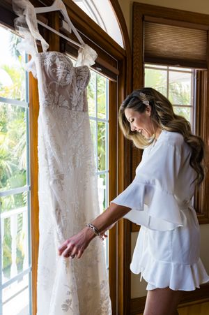 White wedding dress details hanging by sunlit windows in a wooden room.