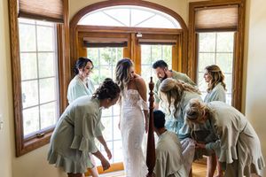 Wedding party getting ready in a room with arched windows and wooden trim.