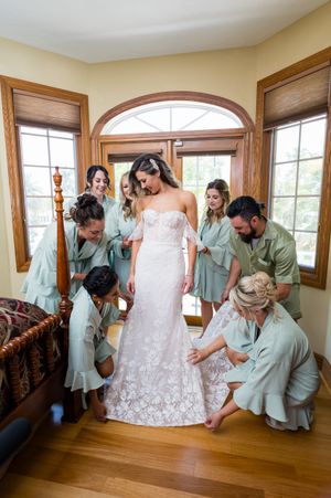 Wedding party in mint green dresses helps with final preparations in a sunlit room.