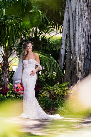 Elegant lace wedding dress photographed in a tropical garden setting with palm trees.