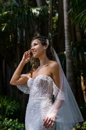 Bride in lace gown poses gracefully in a tropical garden setting.