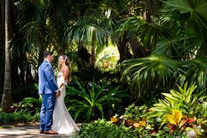 A couple in wedding attire walks through a beautiful tropical garden pathway.