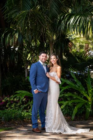 Couple poses among lush tropical garden setting with palm trees.