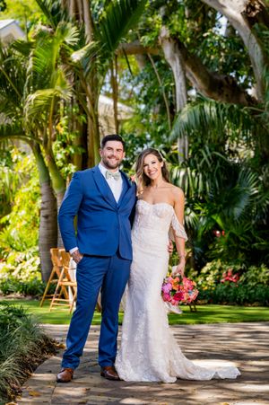 Wedding couple poses in a lush tropical garden setting with palm trees and greenery.