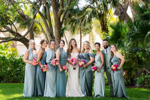 Wedding party in sage green attire poses together outdoors among tropical foliage.