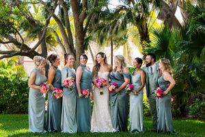 Wedding party in sage green dresses poses outdoors with palm trees in background.
