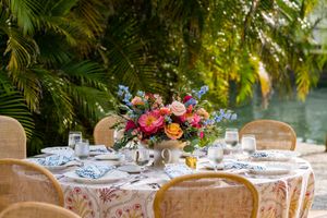 Elegant outdoor wedding reception tables decorated with tropical greenery and floral centerpieces at sunset.