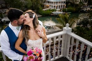 Romantic couple shares a tender kiss on a white balcony overlooking a scenic outdoor venue.