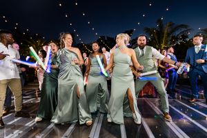 Wedding party dances together on a dance floor at night with glowing lights in the background.