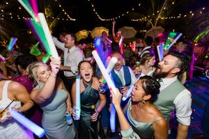 Wedding party guests dancing with colorful LED light sabers on a dark dance floor.