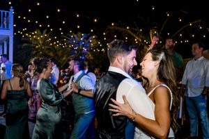 Wedding guests dancing under twinkling lights at an outdoor evening reception.