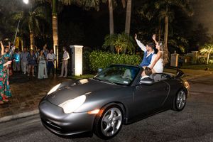 Black sports car parked at night with wedding decorations and guests in background.