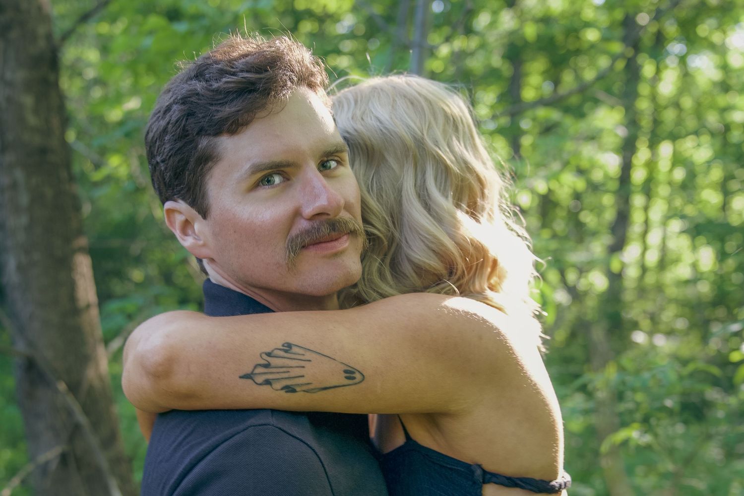 A couple embraces in a romantic moment surrounded by lush green forest scenery.