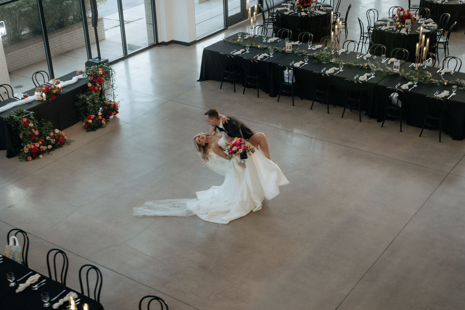 An elegant wedding reception venue setup with white chairs, tables, and floral arrangements in a modern space.