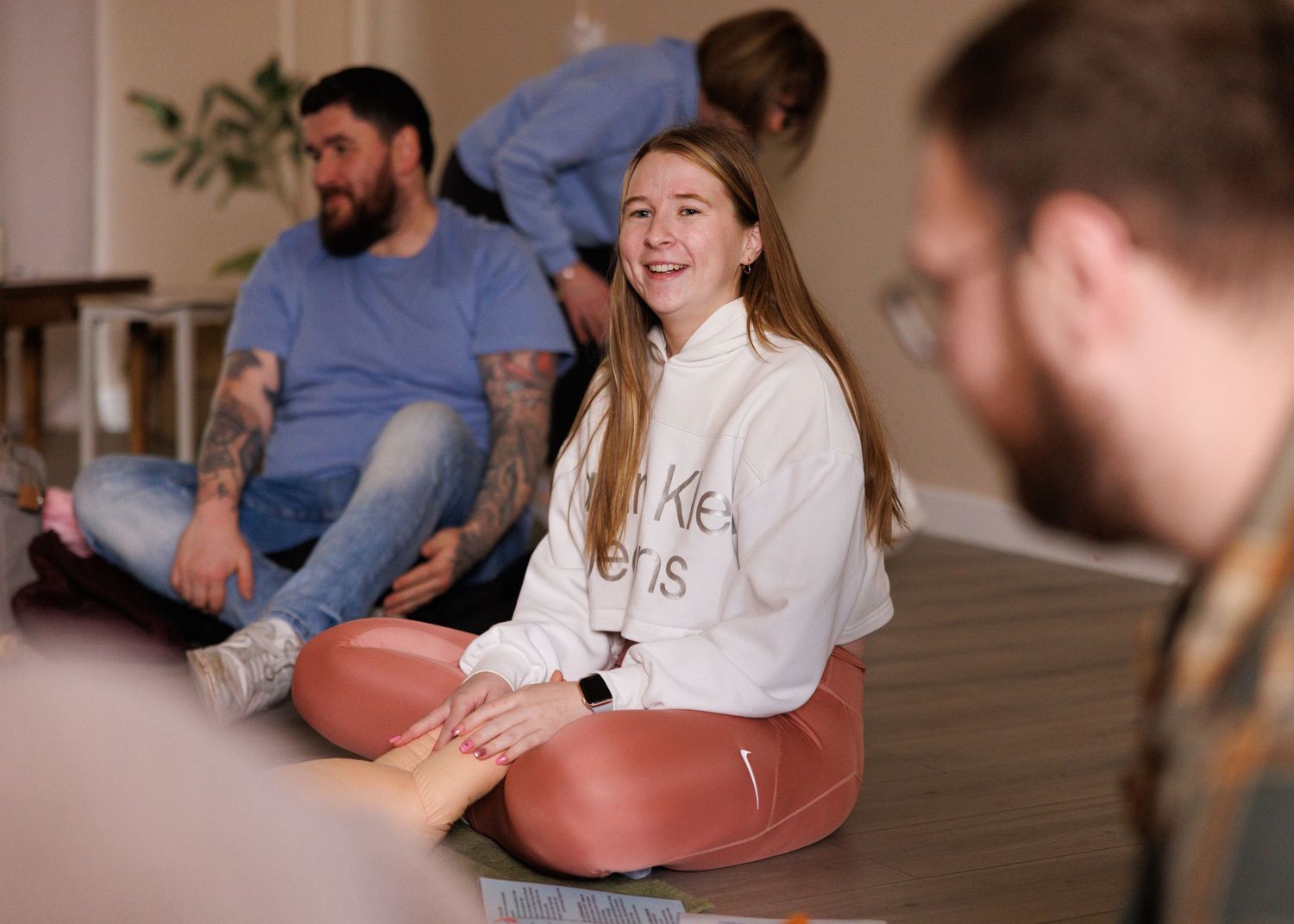 A group sits together on a wooden floor during a casual indoor gathering.