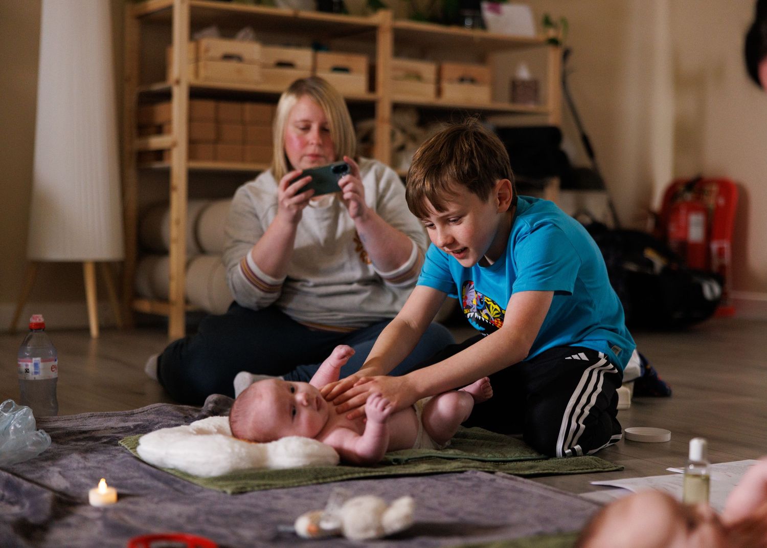 Students practice infant care techniques during a hands-on training session with a baby doll while one documents the lesson.