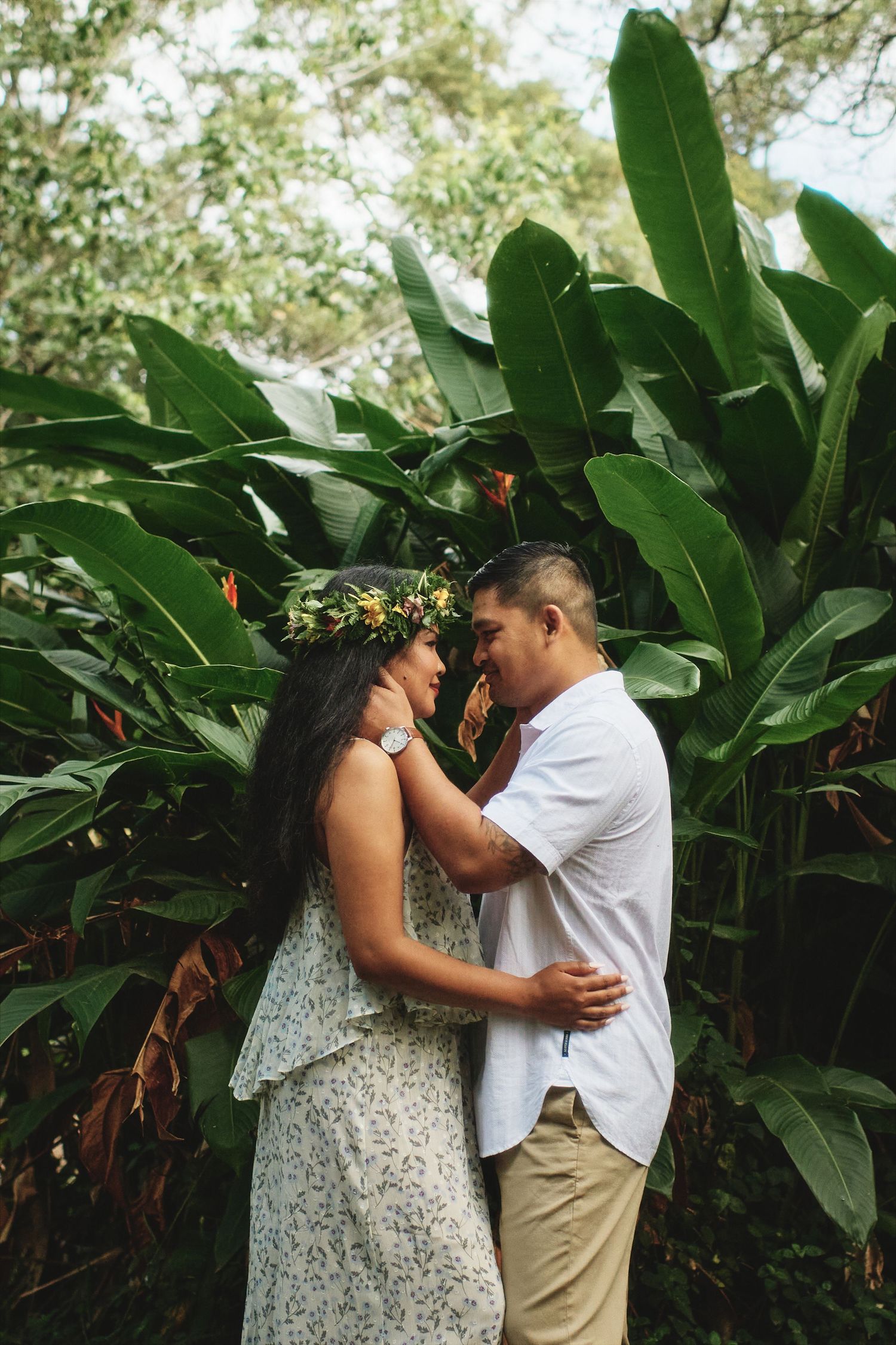 A romantic couple shares an intimate moment among tropical plants during their engagement shoot.