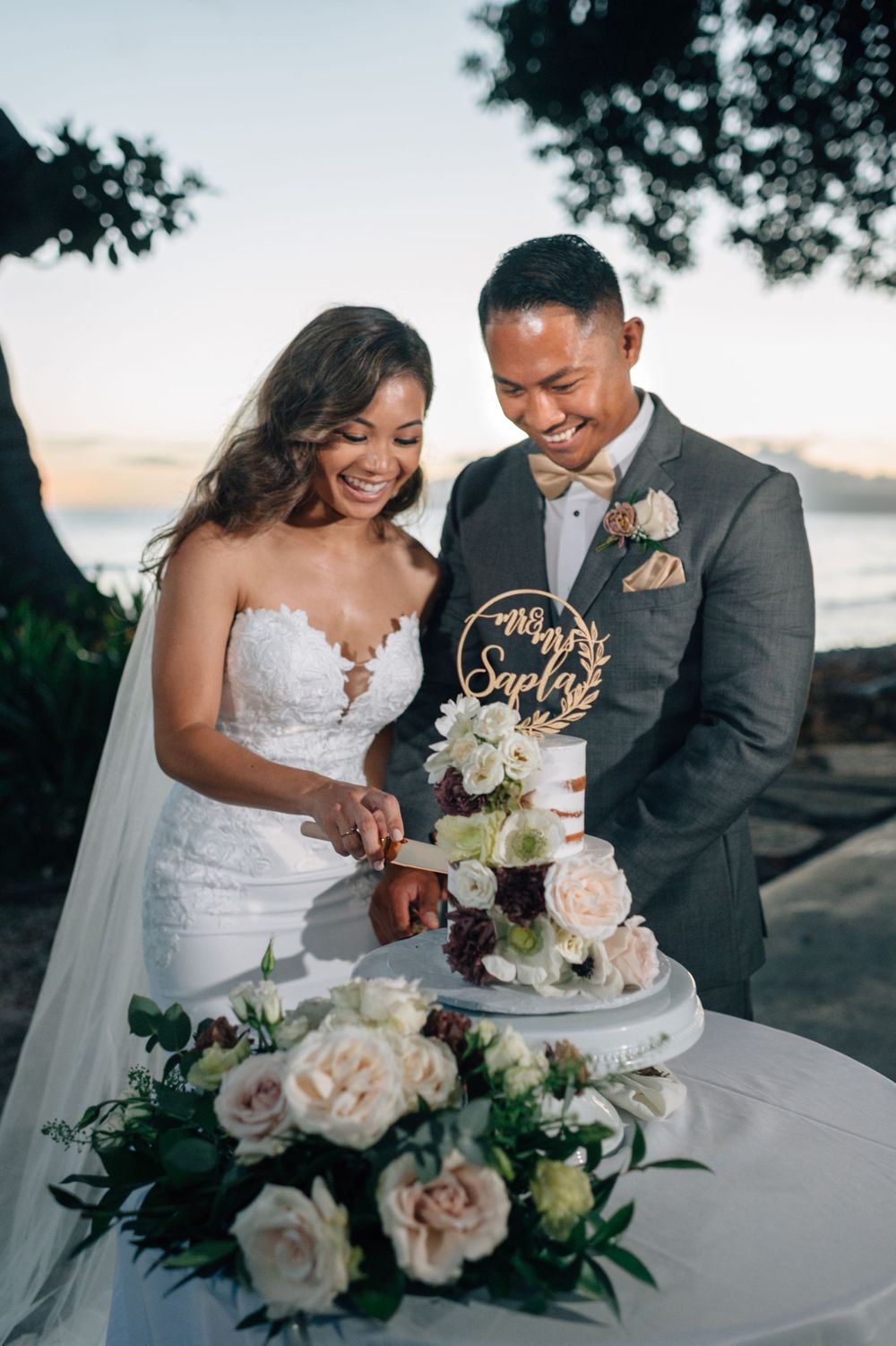 Wedding cake cutting celebration with floral decorations at outdoor reception.