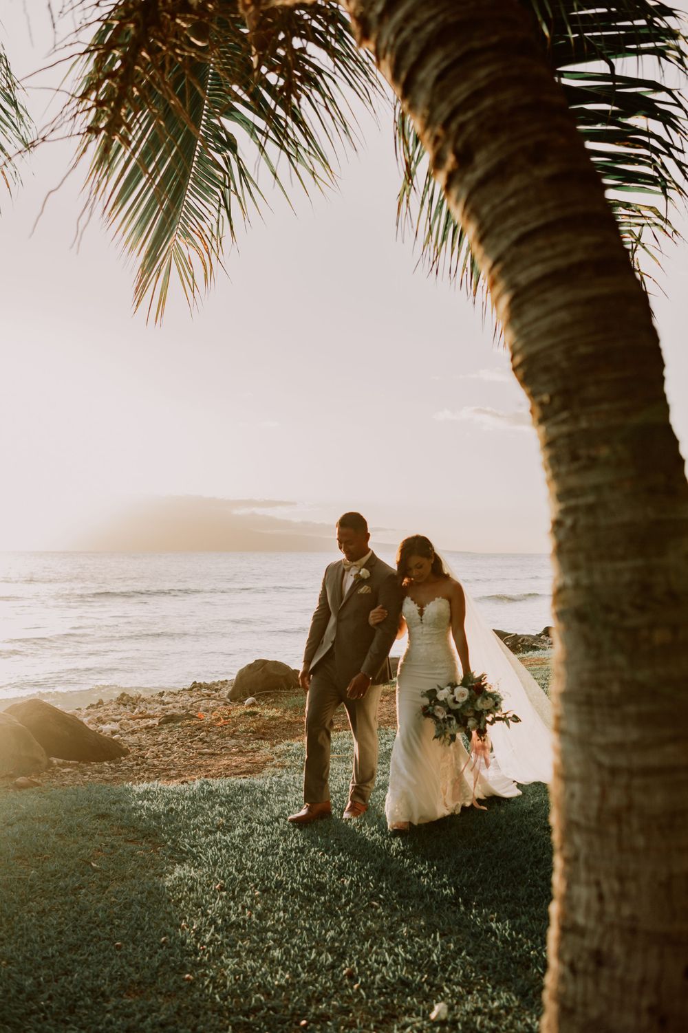 Silhouettes under palm trees during sunset at beach wedding.