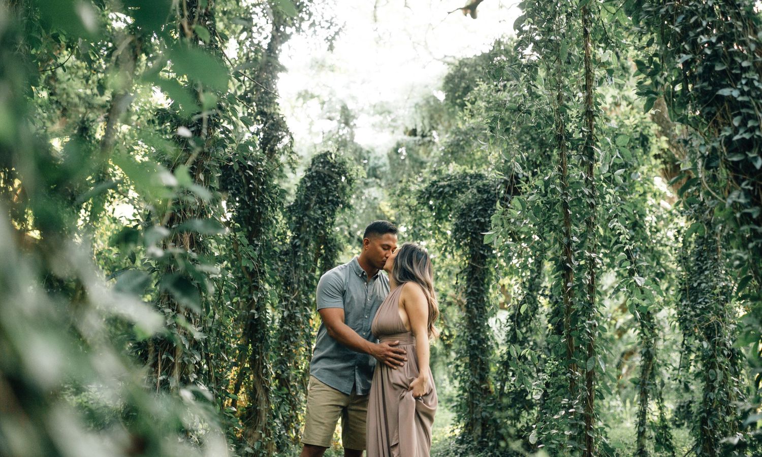 A couple shares tender moments among lush green vines and foliage.