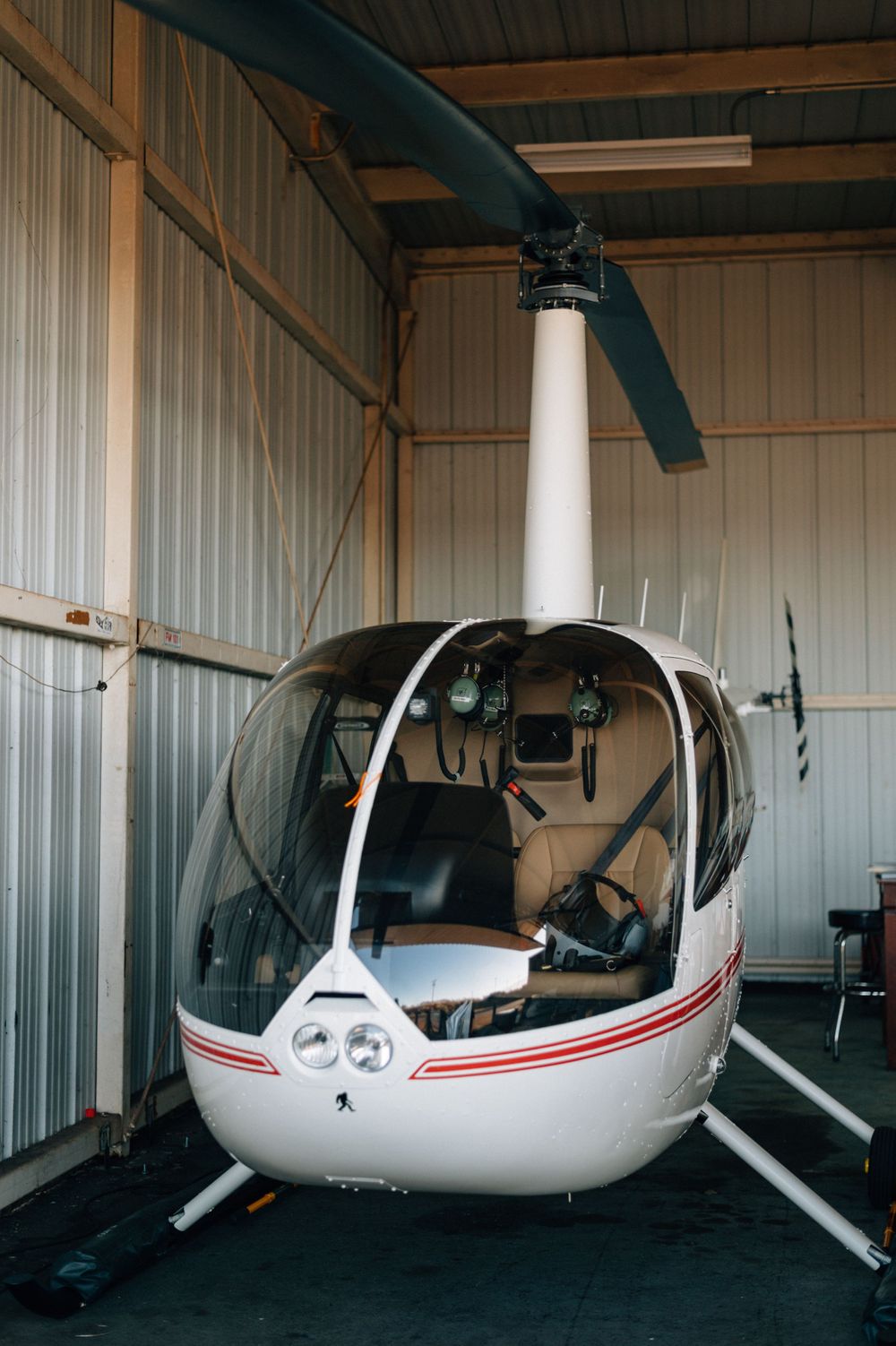 Small white helicopter with red accents stored inside an aircraft hangar.