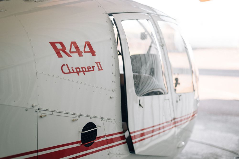 White and red striped small aircraft with R44 designation parked in hangar.
