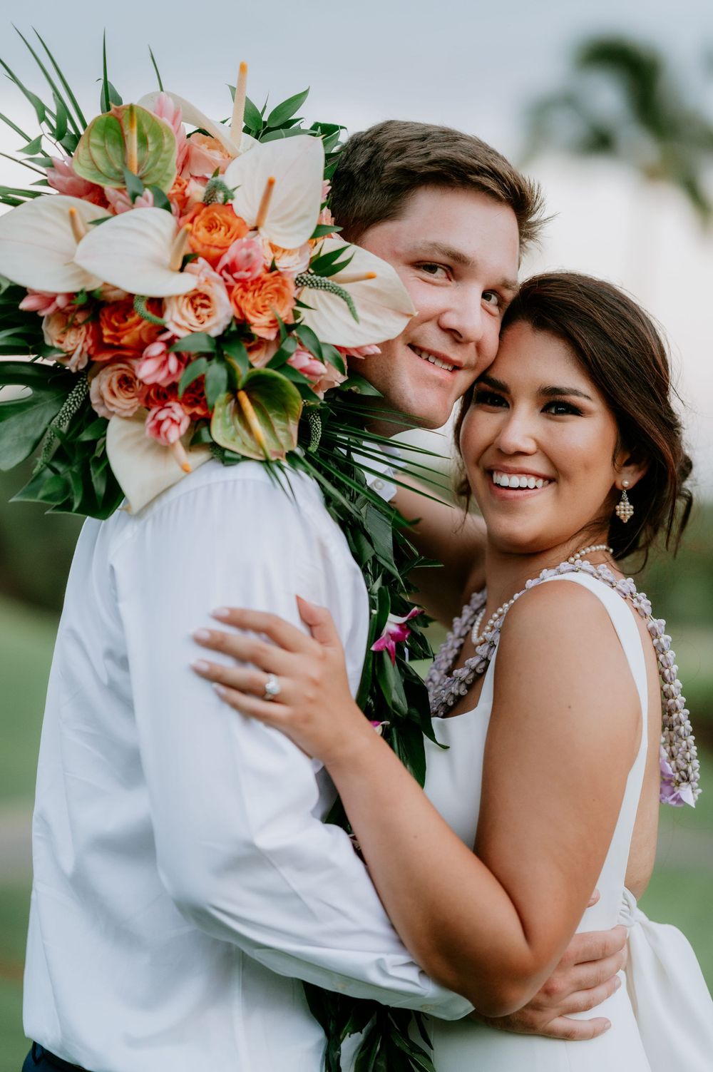 Couple embraces while holding a vibrant coral and peach tropical wedding bouquet.