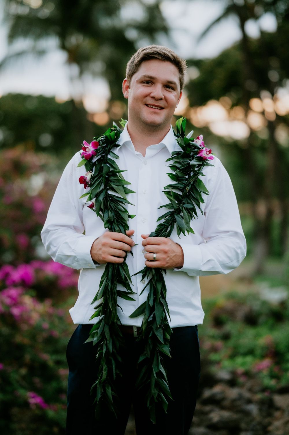 Young attendant wearing traditional Hawaiian maile lei and white shirt at an outdoor ceremony.