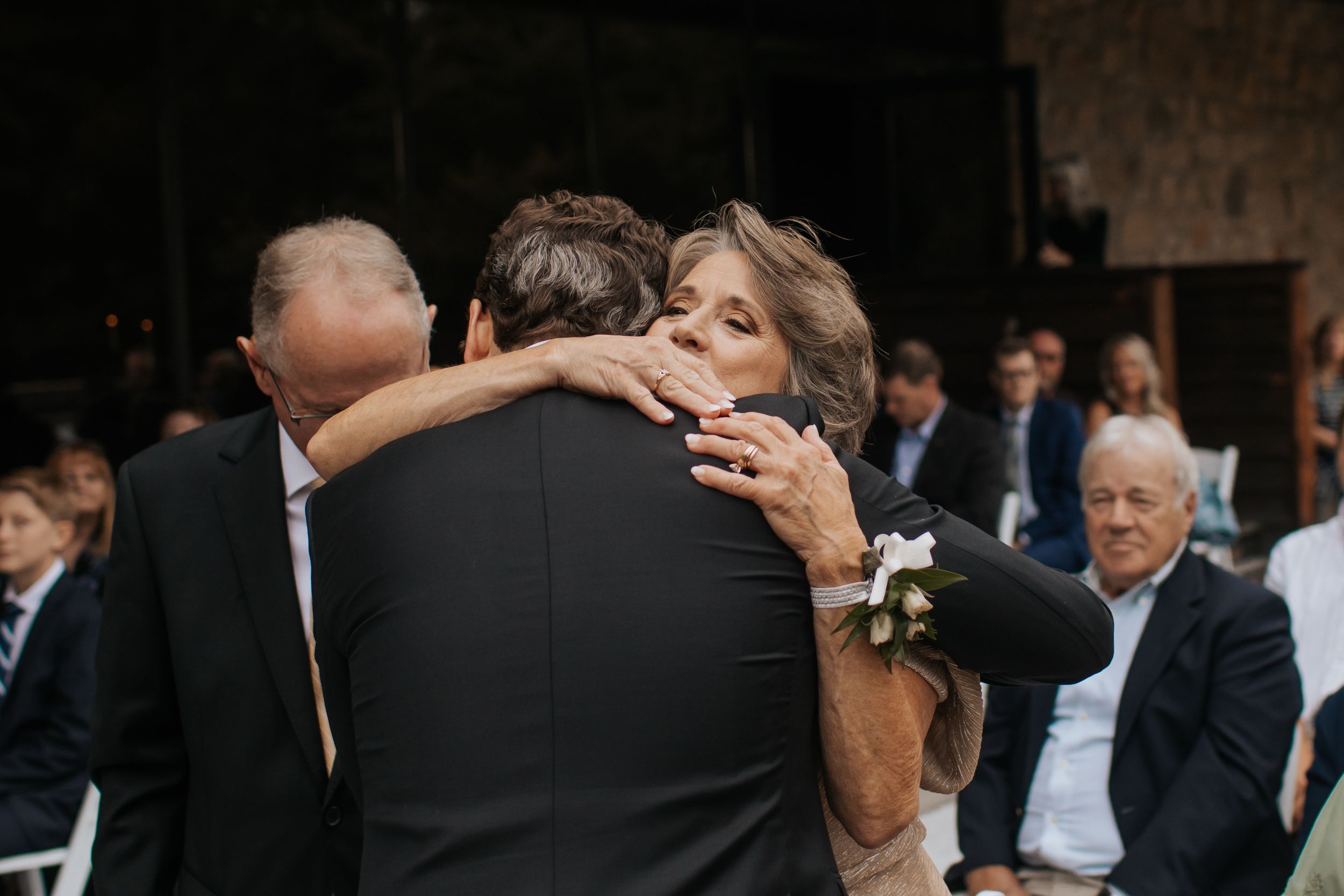 A couple shares an intimate dance at a rustic outdoor wedding reception surrounded by guests.