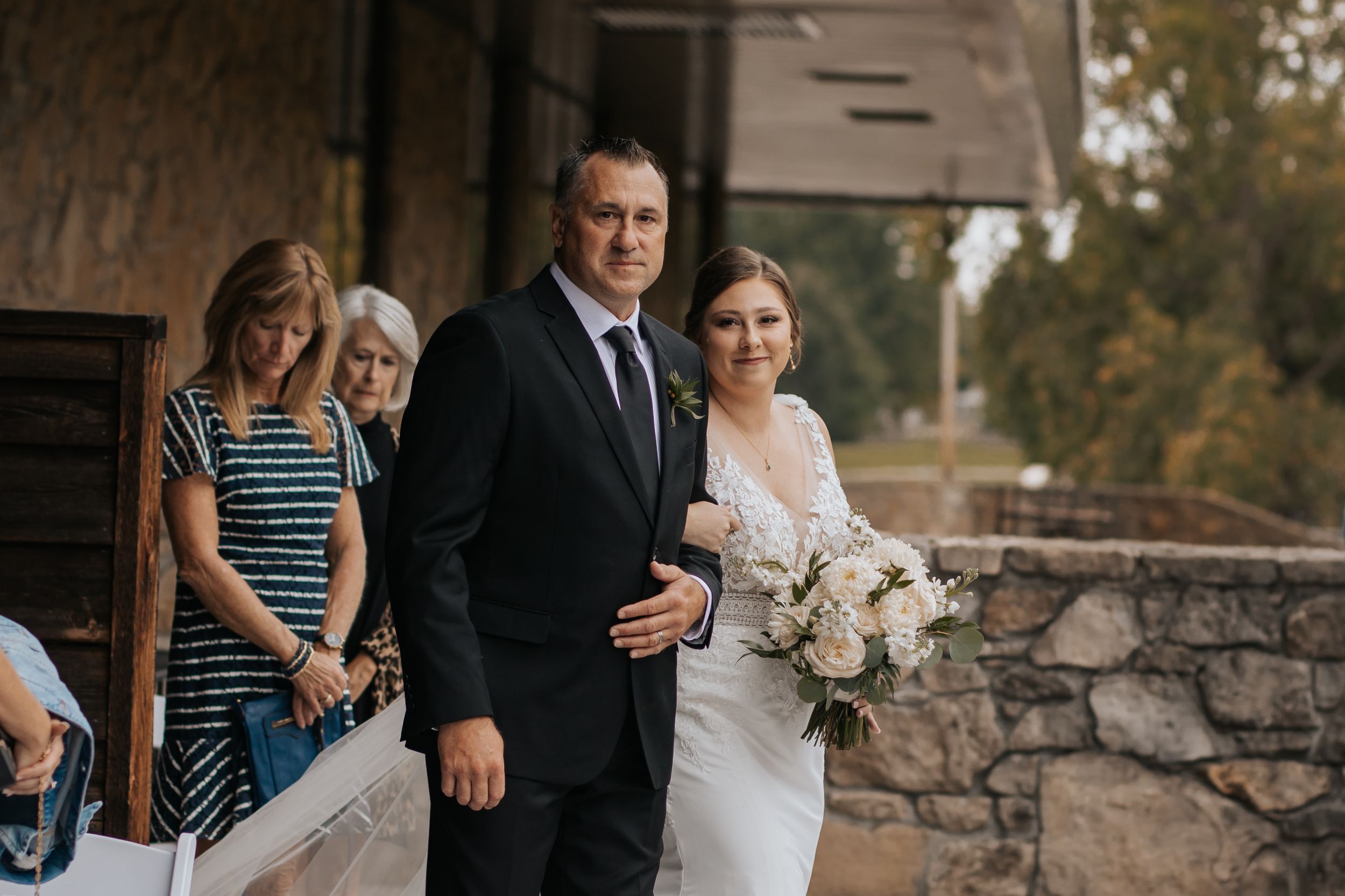 A wedding party stands together on a stone patio during an outdoor autumn ceremony.