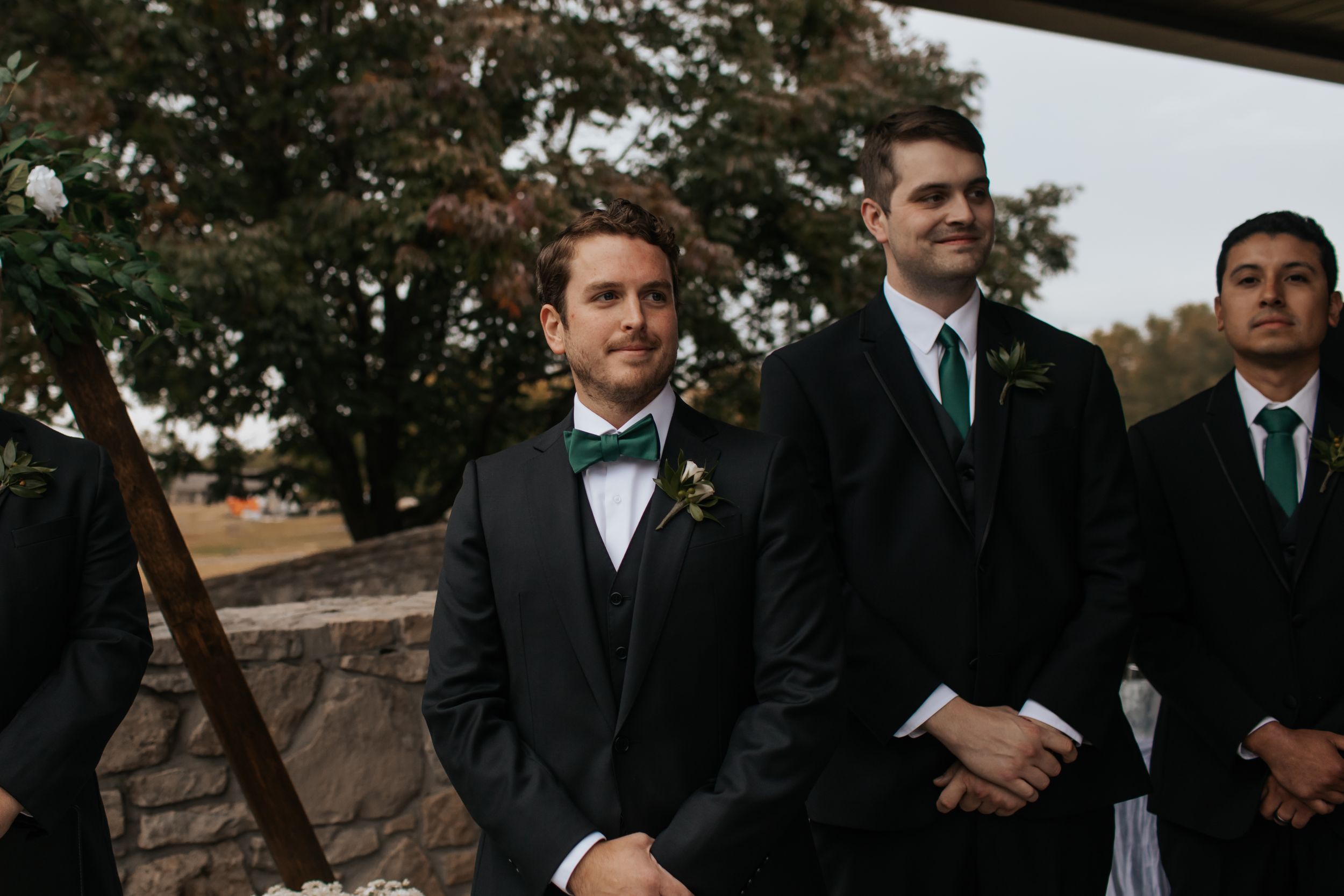 Wedding party members stand together during an outdoor autumn ceremony.