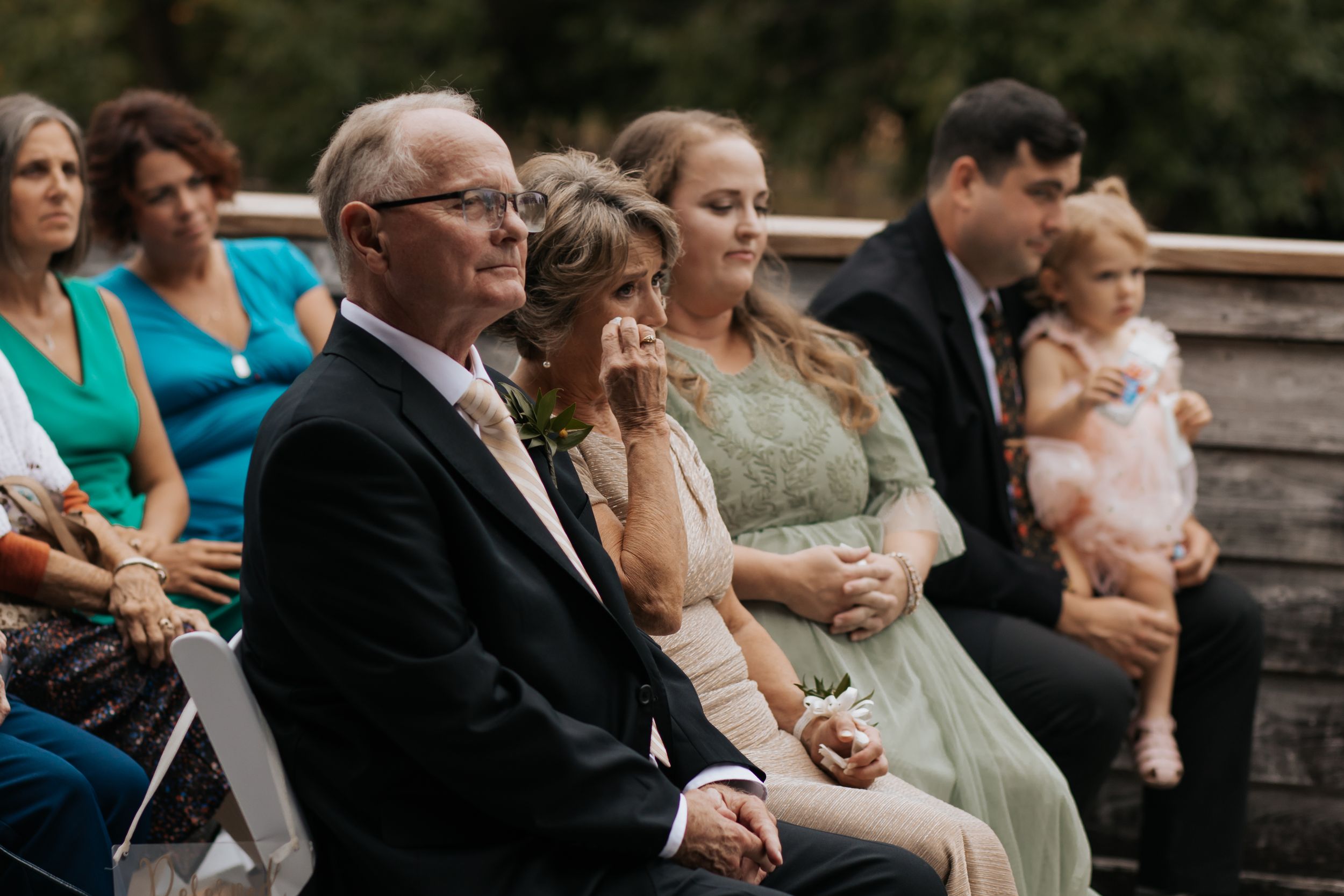 Wedding guests watching the ceremony from white chairs in an outdoor setting.