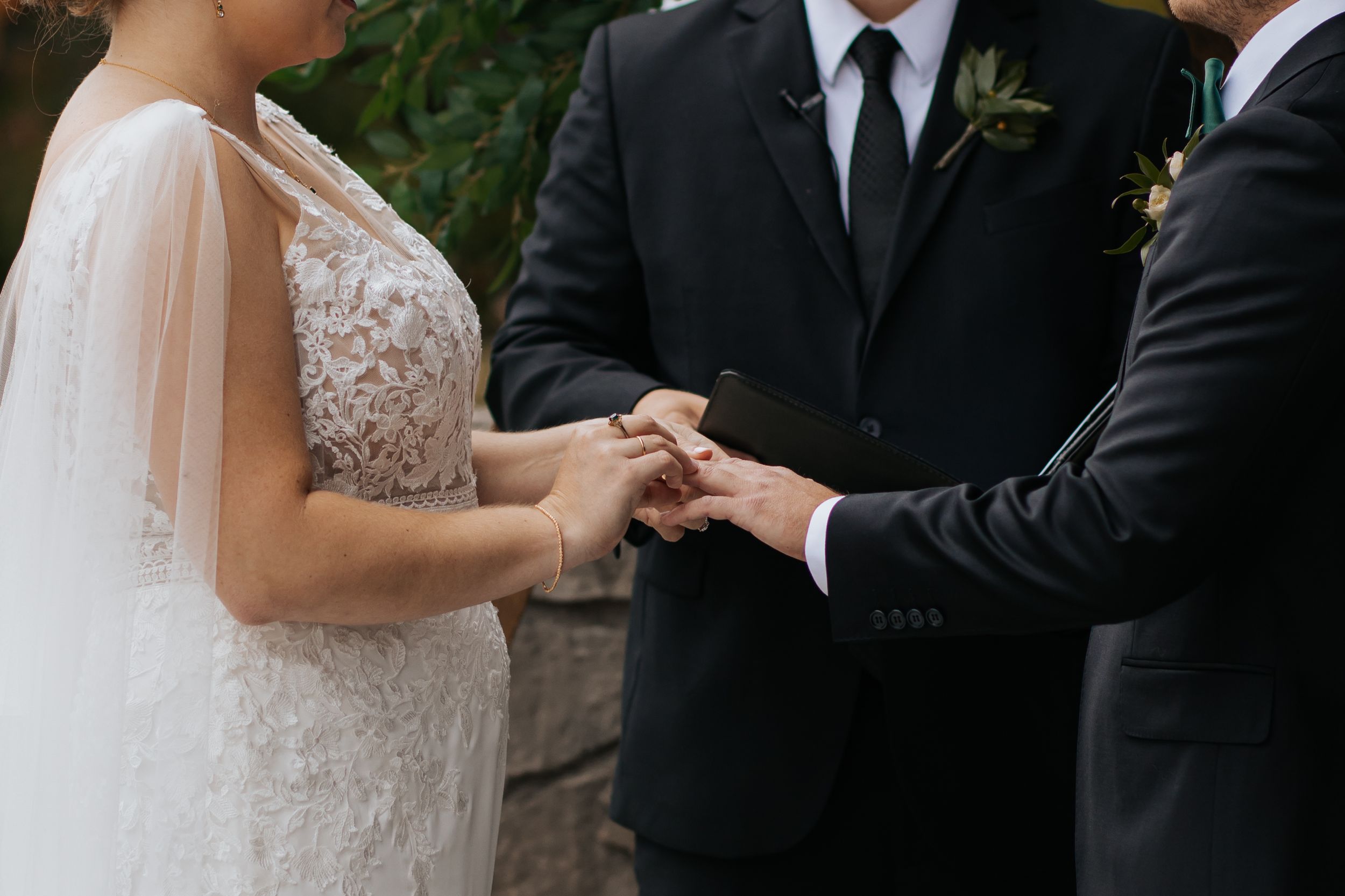 Newlywed couple holds hands during outdoor wedding ceremony with green foliage in background. Conner Prairie, Fishers Indiana