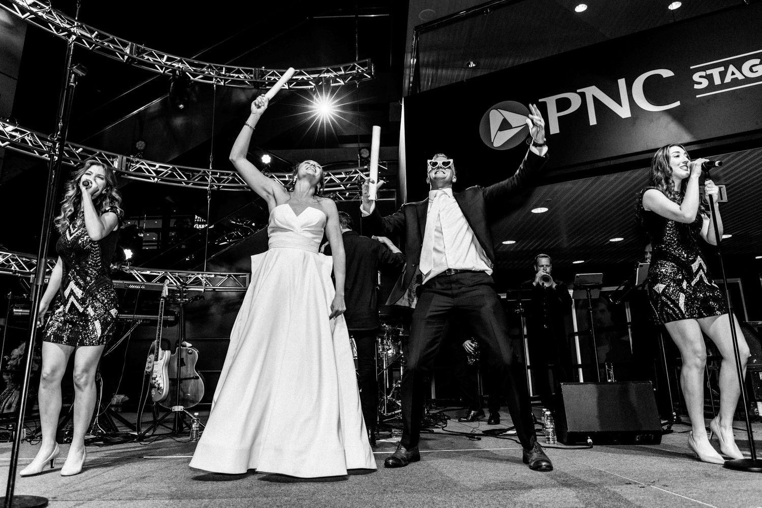 A couple at the Rock and Roll Hall of Fame during their wedding, singing and dancing with a live band on stage.
