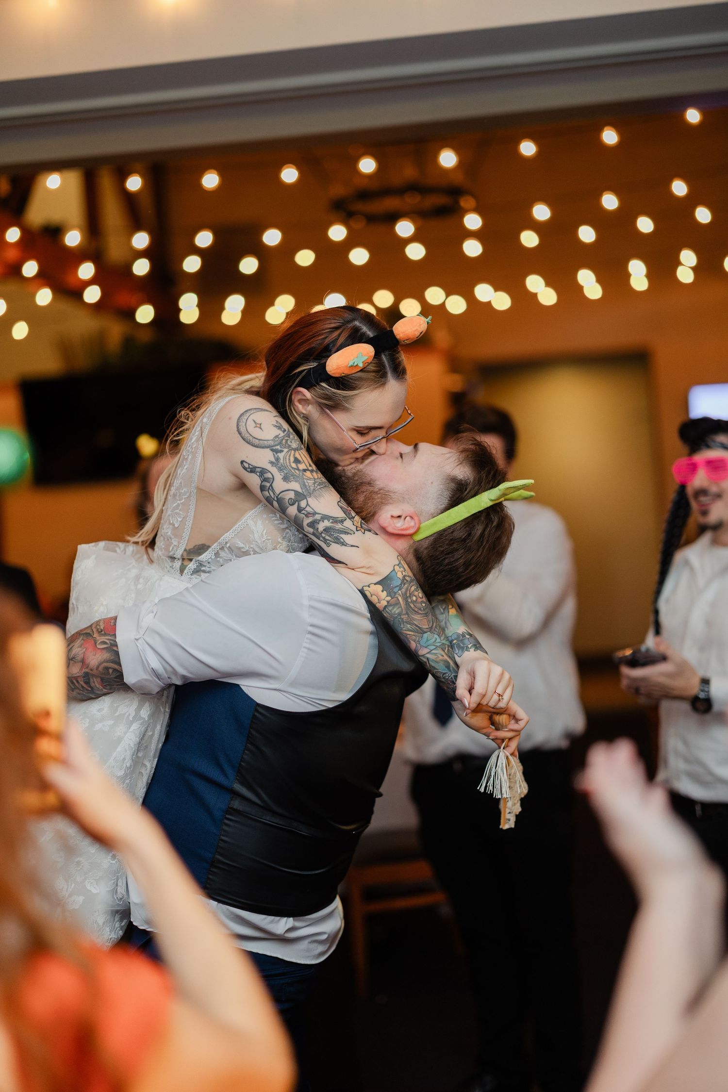 A couple shares a romantic dance moment under twinkling string lights at an indoor wedding reception.