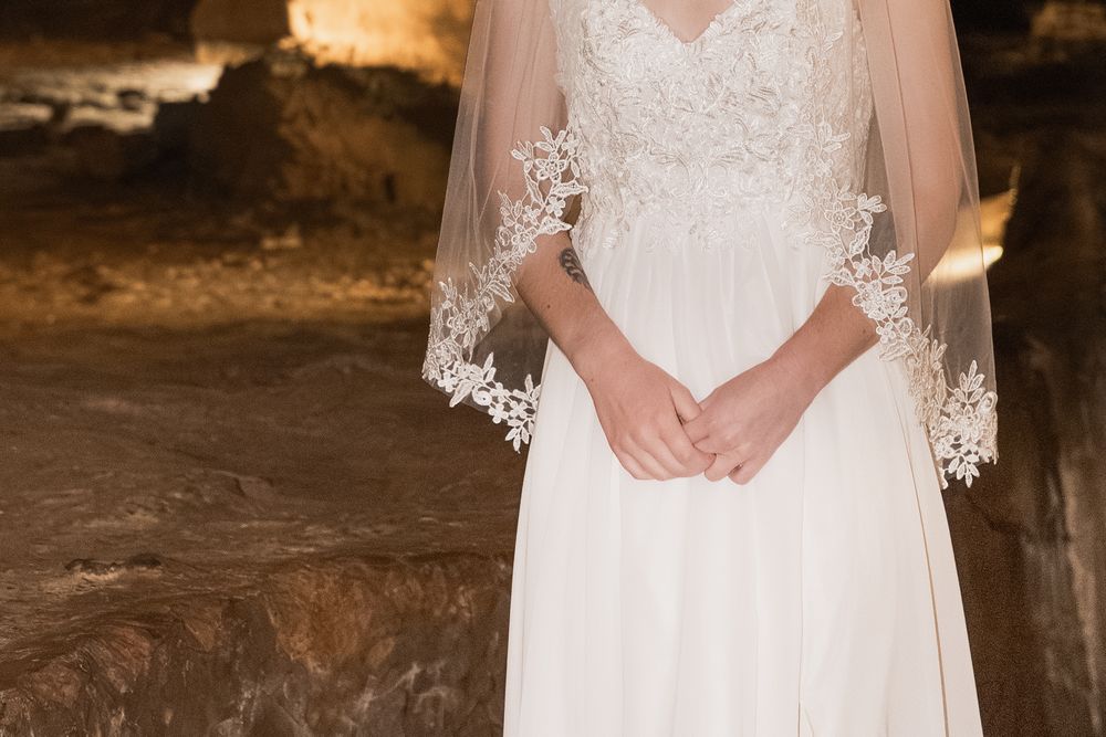 Close-up detail of white lace and beading on a wedding dress against a rustic stone background.