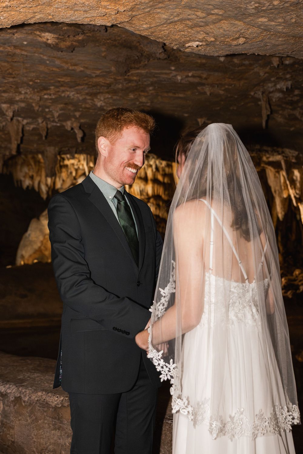 A couple shares an intimate moment during their wedding photos in a dimly lit cave setting.
