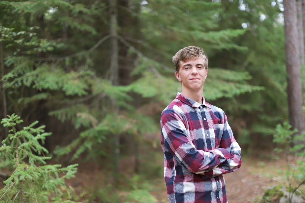 Person in red plaid shirt walking through a lush green forest setting.