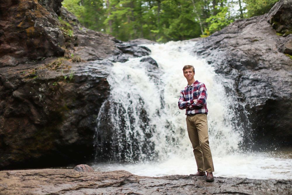Cascading waterfall flows over rocky terrain in a forest setting with someone standing on the rocks.