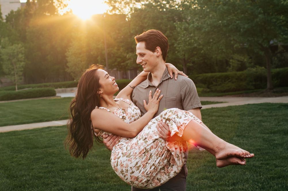A couple embraces on a grassy hill during golden hour sunset in a romantic outdoor photoshoot.