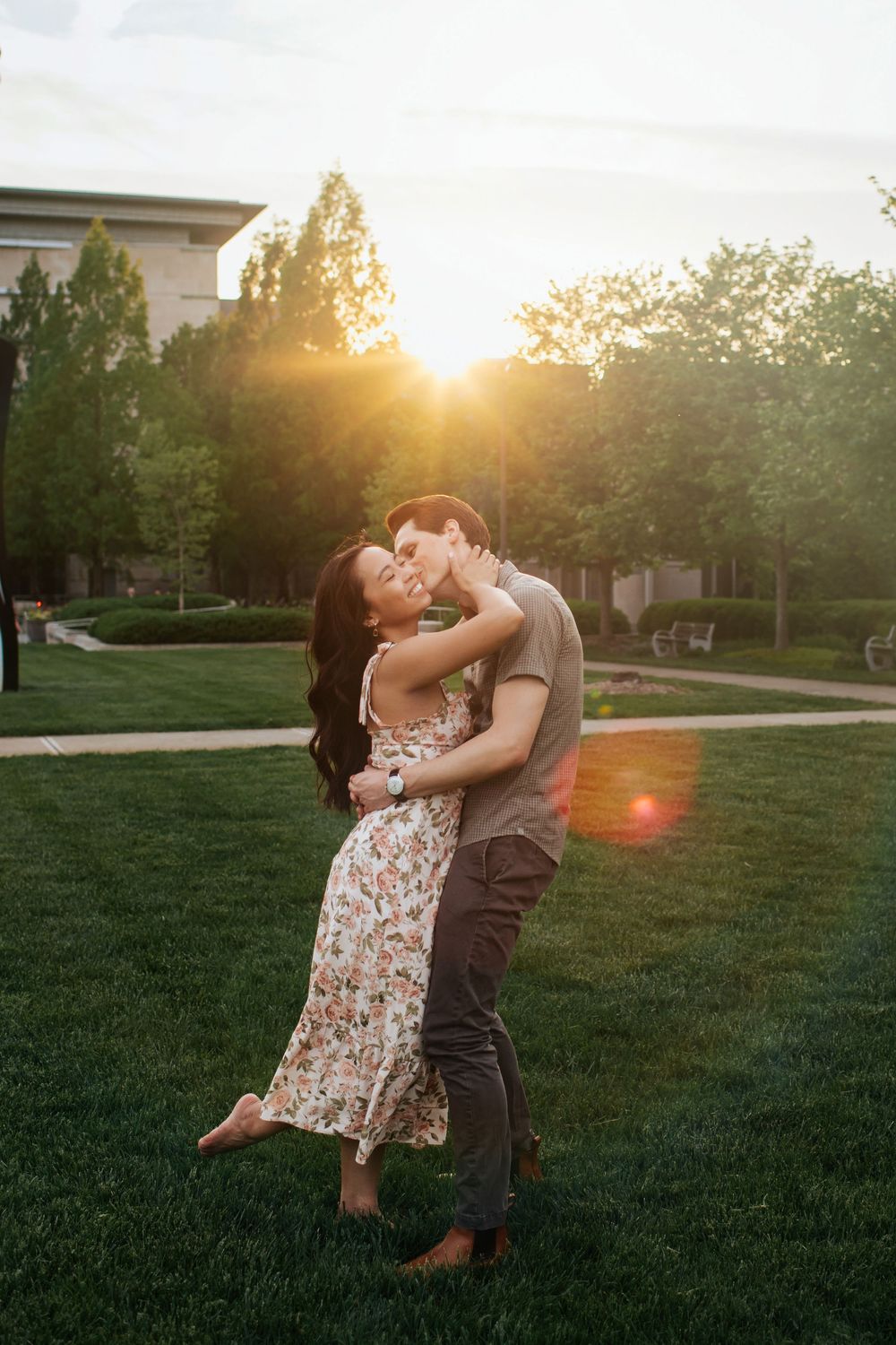 A couple embraces and dances together on a grassy lawn during golden hour sunset.